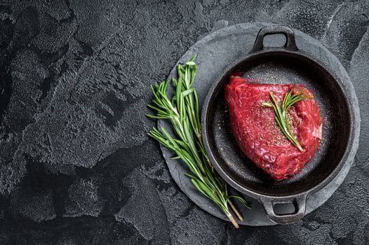 Fresh Raw sirloin rump steak in a skillet with herbs. Black background. Top view. Copy space photo
