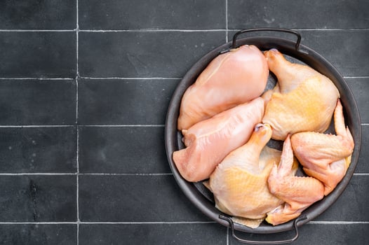 Raw chicken pieces in a metal tray on a black tile background photo