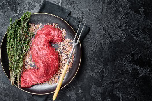 Raw Machete beef meat steak or hanging tender cut on plate with sea salt and thyme. Black background. Top view. Copy space photo