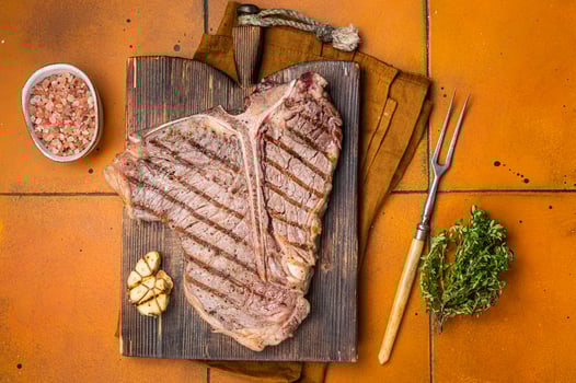 BBQ Roast T bone or Porterhouse beef meat Steak on a wooden board with spices. Orange background. Top view photo