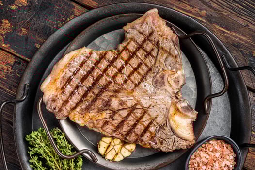BBQ Grilled T-bone or Porterhouse beef meat Steak on a steel tray with herbs. Wooden background. Top view photo