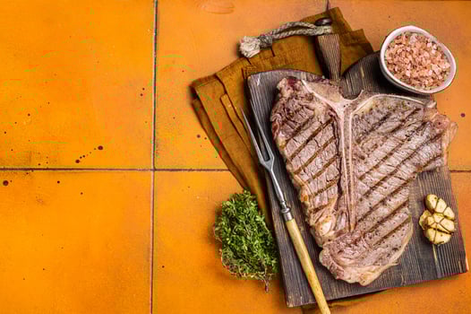 BBQ Roast T bone or Porterhouse beef meat Steak on a wooden board with spices. Orange background. Top view. Copy space photo