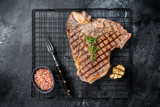 Grilled T-bone or Porterhouse beef meat Steak on a rack. Black background. Top view photo
