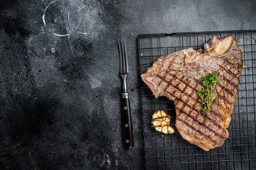 Grilled T-bone or Porterhouse beef meat Steak on a rack. Black background. Top view. Copy space photo