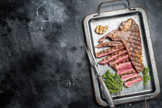Medium rare Grilled T-Bone Steak, Florentine steak sliced in a steel tray. Black background. Top view. Copy space photo
