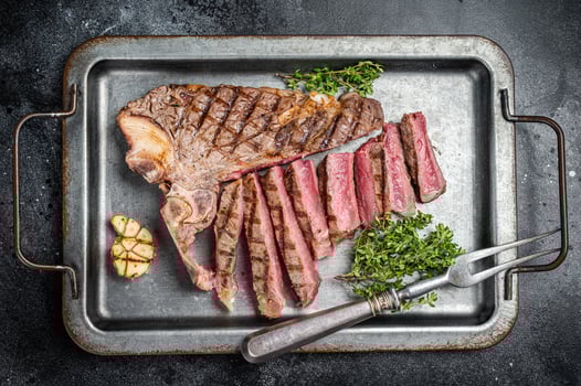 Medium rare Grilled T-Bone Steak, Florentine steak sliced in a steel tray. Black background. Top view photo