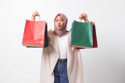 Portrait of attractive Asian hijab woman in casual suit holding and showing colorful paper shopping bags. Shopaholic girl and discount buying concept. Isolated image on white background photo