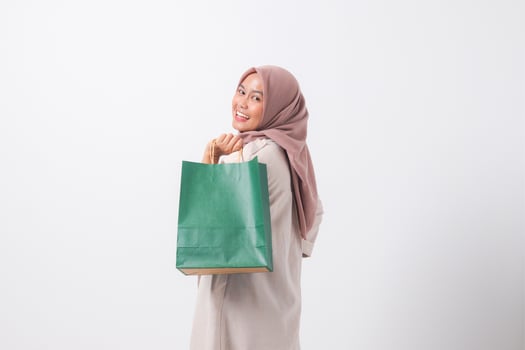 Portrait of cheerful Asian hijab woman in casual suit holding and showing colorful paper shopping bags. Shopaholic girl and discount buying concept. Isolated image on white background photo