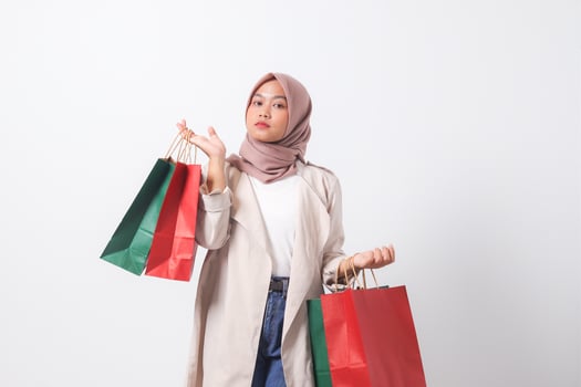 Portrait of cheerful Asian hijab woman in casual suit holding and showing colorful paper shopping bags. Shopaholic girl and discount buying concept. Isolated image on white background photo