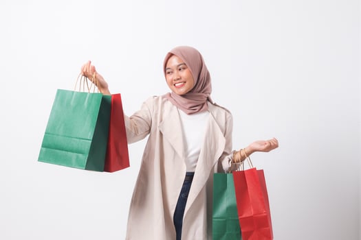 Portrait of attractive Asian hijab woman in casual suit holding and showing colorful paper shopping bags. Shopaholic girl and discount buying concept. Isolated image on white background photo