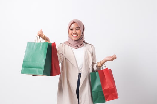 Portrait of attractive Asian hijab woman in casual suit holding and showing colorful paper shopping bags. Shopaholic girl and discount buying concept. Isolated image on white background photo