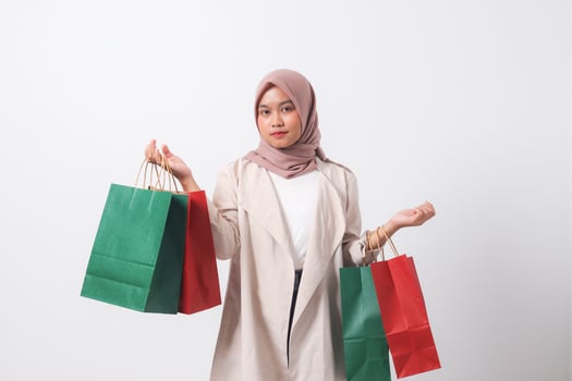 Portrait of attractive Asian hijab woman in casual suit holding and showing colorful paper shopping bags. Shopaholic girl and discount buying concept. Isolated image on white background photo