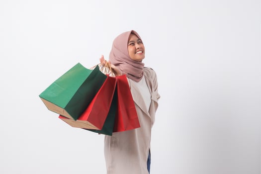 Portrait of excited Asian hijab woman in casual suit holding and showing colorful paper shopping bags. Shopaholic girl and discount buying concept. Isolated image on white background photo