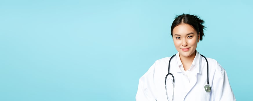 Healthcare and medical concept. Korean female doctor, nurse in uniform, smiling and looking helpful, blue background photo