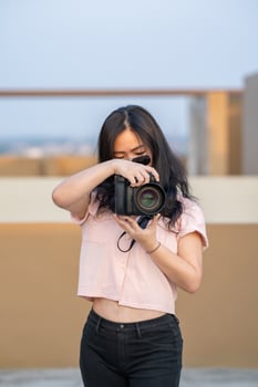 Amateur sunglasses Asian Woman take a photo with professional mirrorless camera at outdoor blue rooftop building in twilight time.
