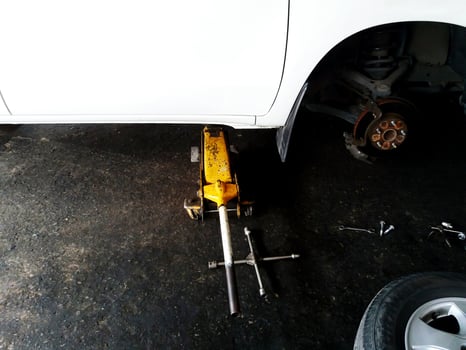 Yellow car lift jack lifting white car during fixing, maintenance or change new brake with half of tire at garage with copy space photo