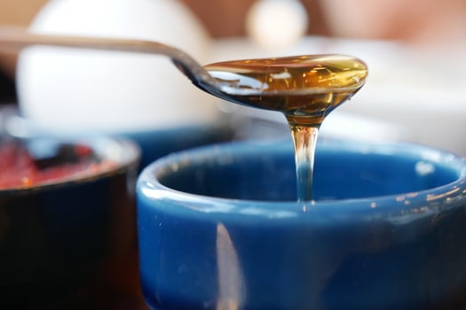 Golden Honey is Dripping Lavishly from the Spoon into the Blue Bowl photo