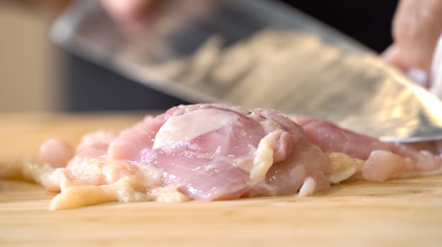 A chef using a kitchen knife slices uncooked chicken meat on a chopping board, the close up view of preparing food ingredients. photo