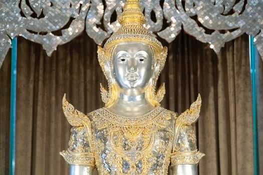 Deity statue standing straight made of silver, wearing silver gold costume with Chada on top of his head. Surrounded by sparkleling decoration. photo