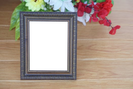 Photo frame on wooden floor, decorated with flowers behind. Copy space for adding text or photos. Concept, Proud, memories and nostalgia. Exhibition, art gallery. Photography.