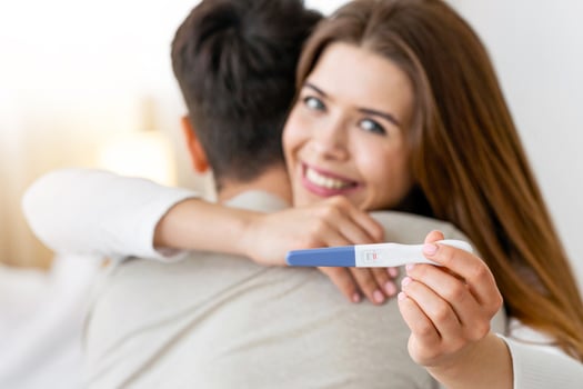 Focus on pregnancy test. Young husband and wife hugging at home photo