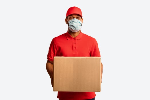 African American Delivery Man Holding Cardboard Box Delivering Postal Package Wearing Medical Mask During Coronavirus Pandemic Over Yellow Studio Background. photo