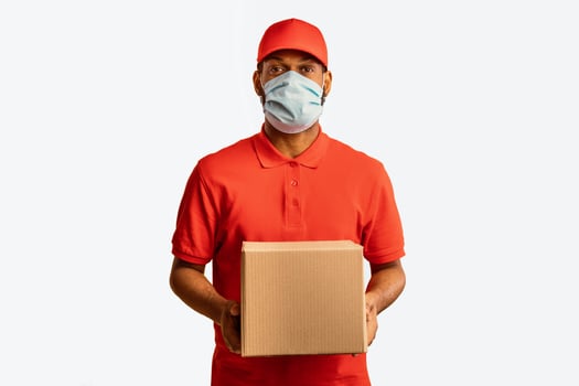 Delivery Service. Black Courier Guy Delivering Cardboard Box Holding Package Wearing Mask During Coronavirus Quarantine Standing Over Yellow Studio Background. photo