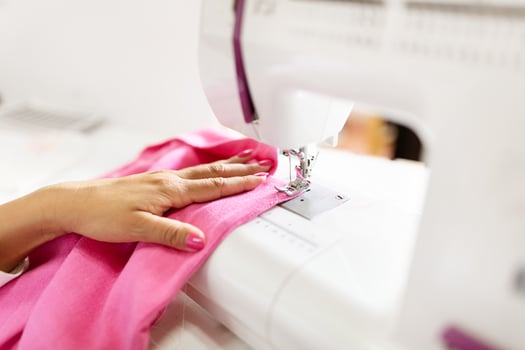 A mature Hispanic woman focuses intently as she sews pink fabric at her office desk. She demonstrates skill and creativity in her design work, surrounded by tools and materials. photo