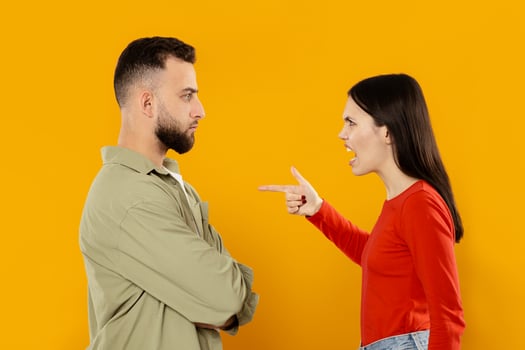 A young couple stands facing each other in a tense moment. The woman appears upset, pointing her finger at the man, who has a serious expression while crossing his arms. photo