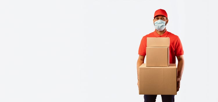 African Delivery Man Holding Boxes Wearing Medical Mask Standing Over Yellow Studio Background. Safe Shopping And Delivery. Panorama, Copy Space photo