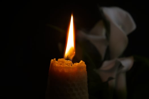 Burning wax candle and white calla lily flowers in darkness photo