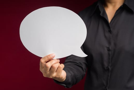 Text speech bubble concept. Close-up of hand holding a white speech bubble against a red background photo