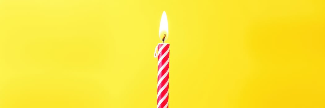 Bright red and white striped birthday candle burning against a vibrant yellow background at a festive celebration photo