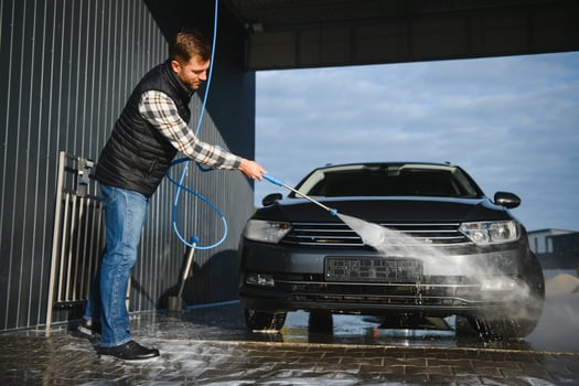 A man washes his car at a self service car wash using a hose with pressurized water. photo