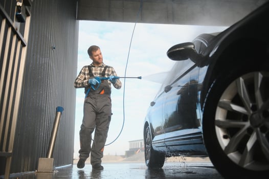 Man worker in uniform washing standing front car service station. Car wash cleaning station photo