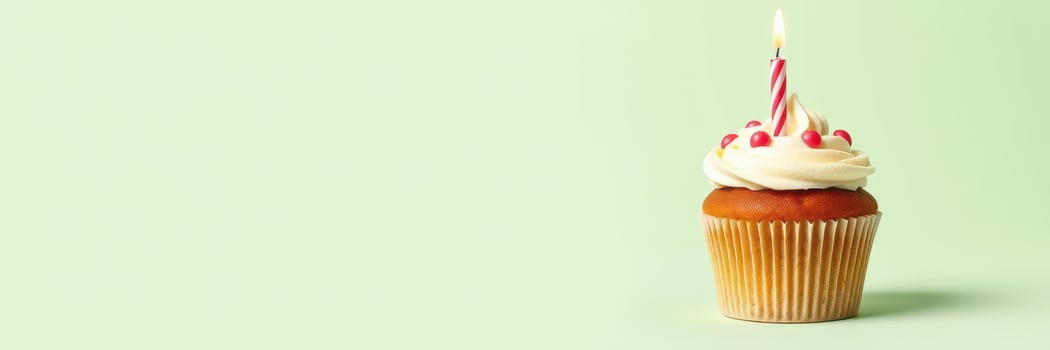 Colorful cupcake with white frosting and a candle stands on a green background for a birthday celebration photo