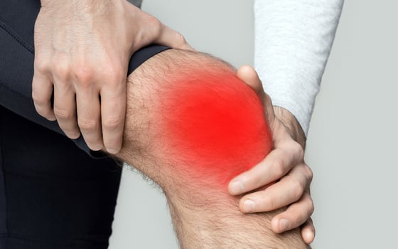 Knee injury or inflammation. Man in sportswear presses his hands to knee highlighted in red, close up, cropped, studio shot photo