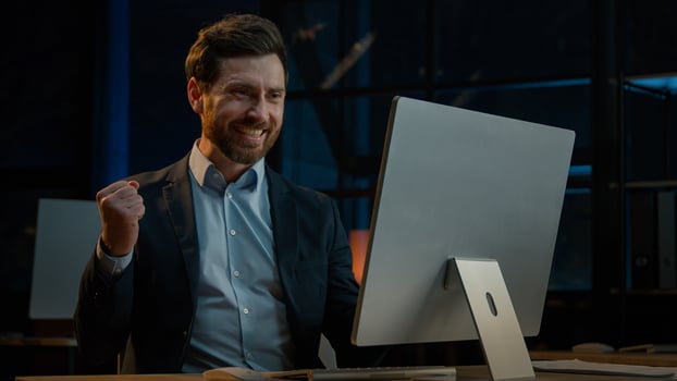 Middle-aged 40s businessman entrepreneur winner Caucasian man investor developer sit at dark evening office business company work on computer rejoice victory celebrate triumph achieve profit success photo