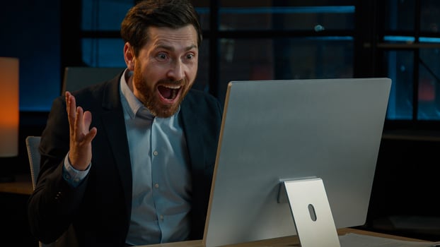 Happy Caucasian man middle-aged senior businessman adult investor broker salesman manager work with computer indoors dark night office win job offer good news winning online bet profit rejoice victory photo