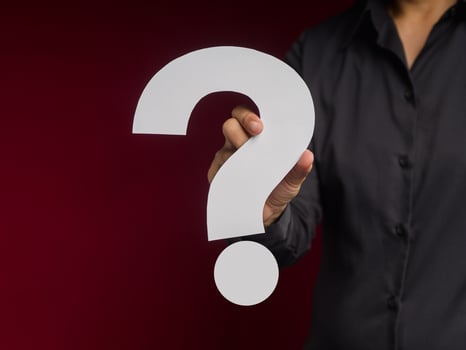 Businessman holding a white question mark paper while standing over a red background photo