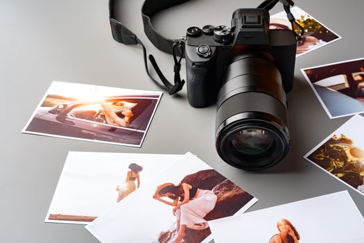 Photo camera with colorful printer photos on gray desk