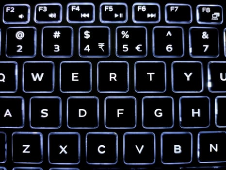 A close-up of a backlit keyboard with illuminated keys in a QWERTY layout. White letters on black keys contrast sharply, showcasing a sleek, modern design with a smooth, polished finish. photo