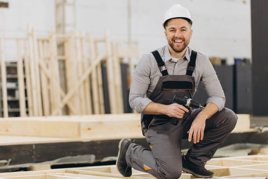 Carpenter kneeling and holding cordless drill in modular building workshop photo