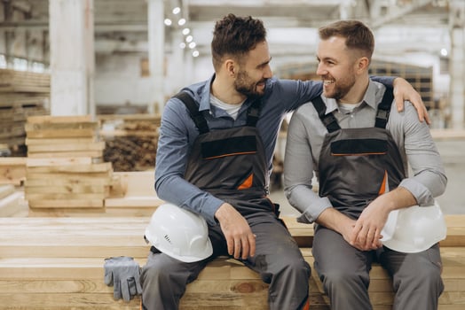 Two happy carpenters resting on wood planks in lumber warehouse photo