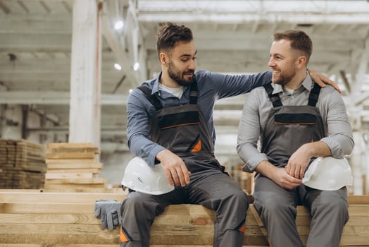 Two carpenters resting and chatting on wooden planks in workshop photo