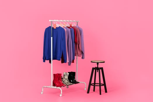 Stylish clothing and boots on a rack. Symbol of modern consumerism while shopping for trendy outfits, pink studio background photo