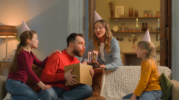 Happy birthday event Caucasian family mom children congratulate dad surprise birth party cheerful parents little girls kids daughters siblings festive caps celebrate blowing candles cake together home photo