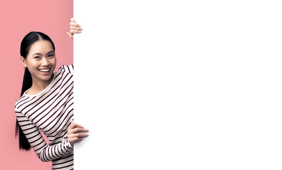 Positive Young Asian Woman Standing Near Big White Advertisement Board, Smiling Korean Lady Demonstrating Free Copy Space On Blank Billboard For Your Design Or Offer, Standing Over Pink Background photo