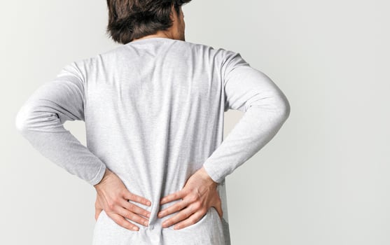 Body ache and kidneys pain. Man presses his hands to back, isolated on gray background, studio shot photo