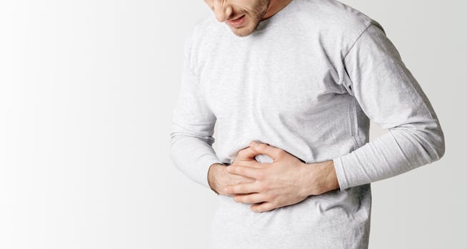 Stomach problems and body ache. Young man presses his hands to stomach in pain, panorama, cropped, studio shot photo